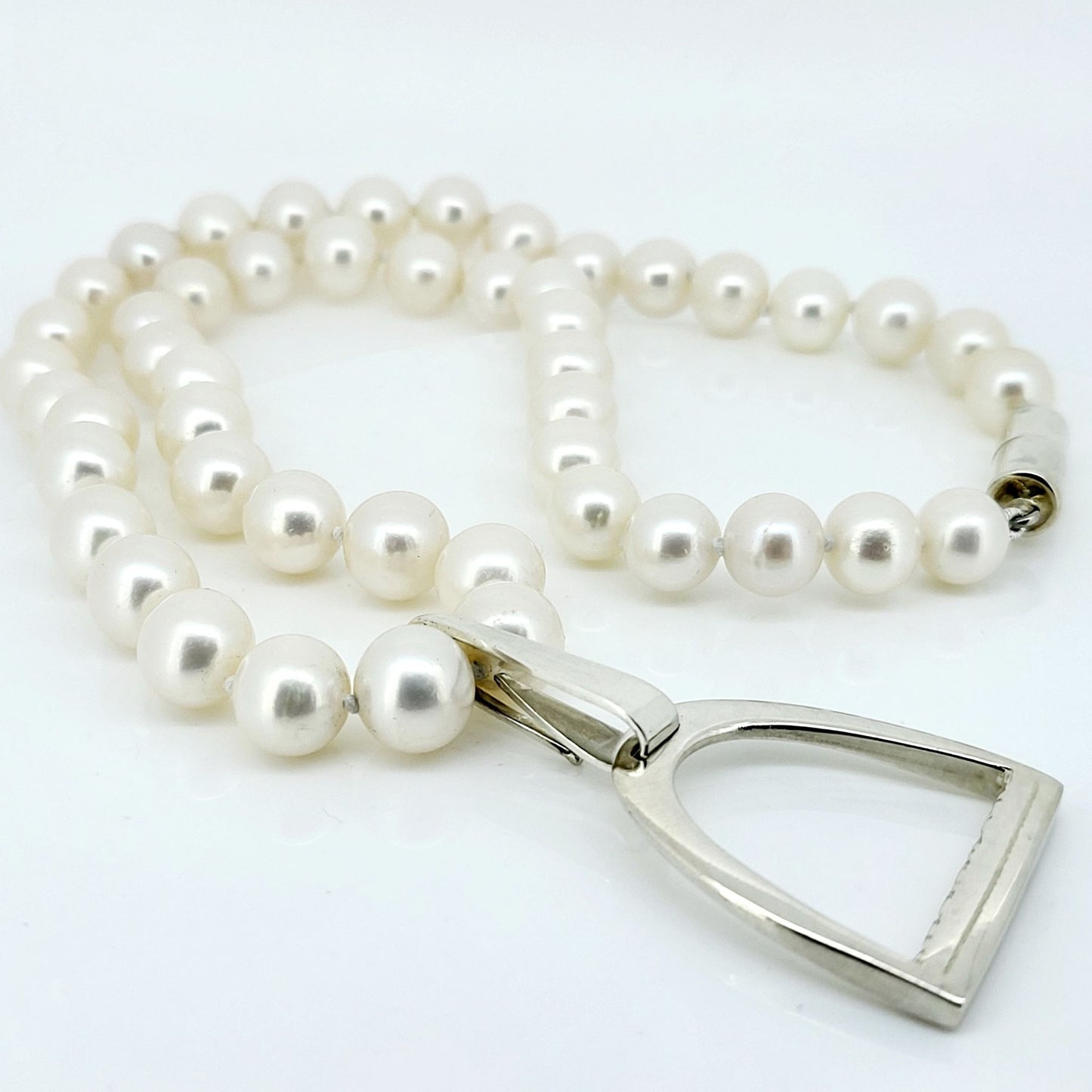 This is a photo of a large Stirrup Pendant, made from sterling silver, attached to a string of white pearls made by Crawford Hill Equestrian Jewellery.