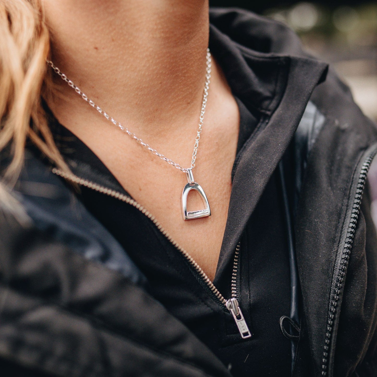 Person wearing a black jacket with a silver medium horse stirrup necklace.