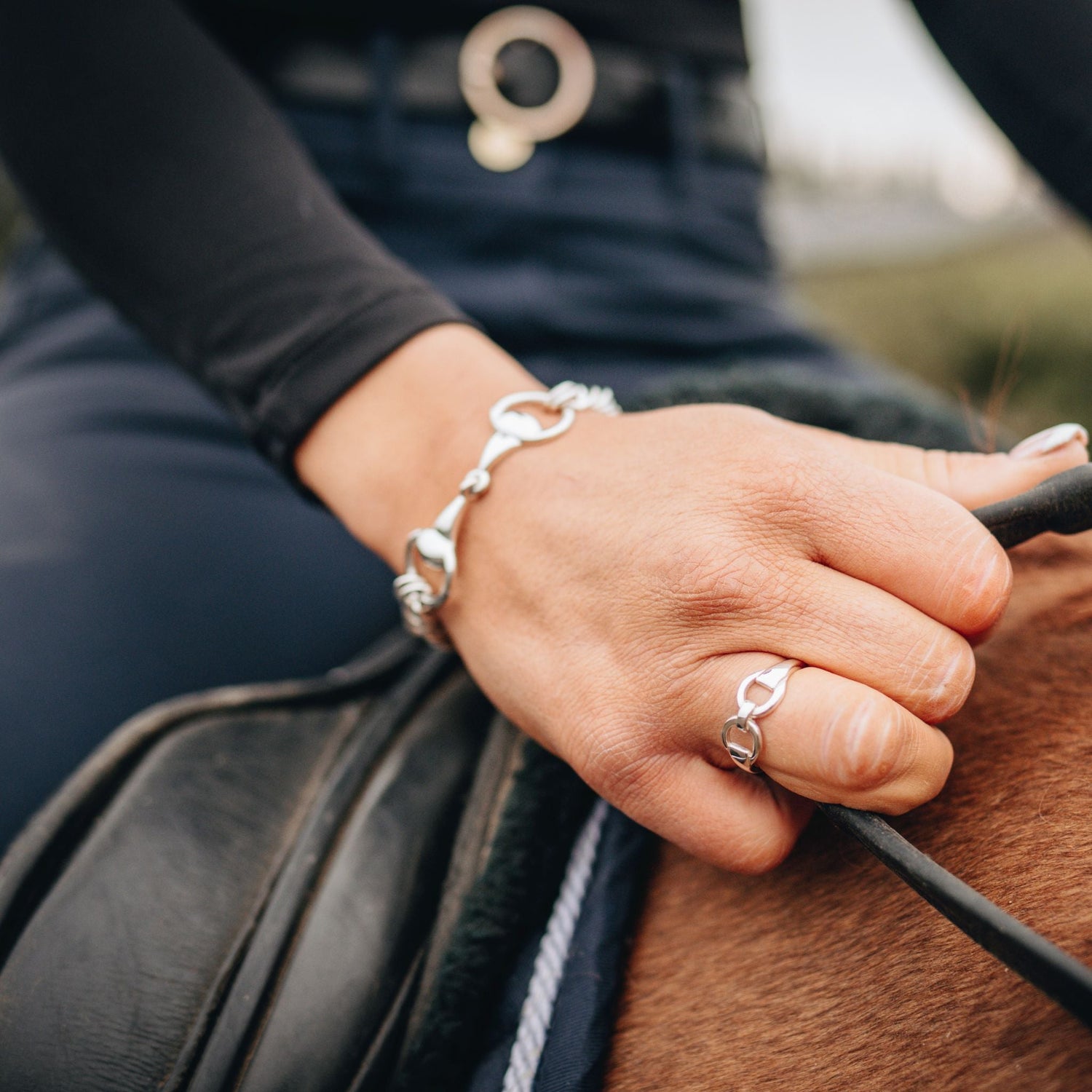 A photo of a horse rider holding the reins wearing a crawford hill snaffle curb chain beacelet and a horse bit snaffle ring. 