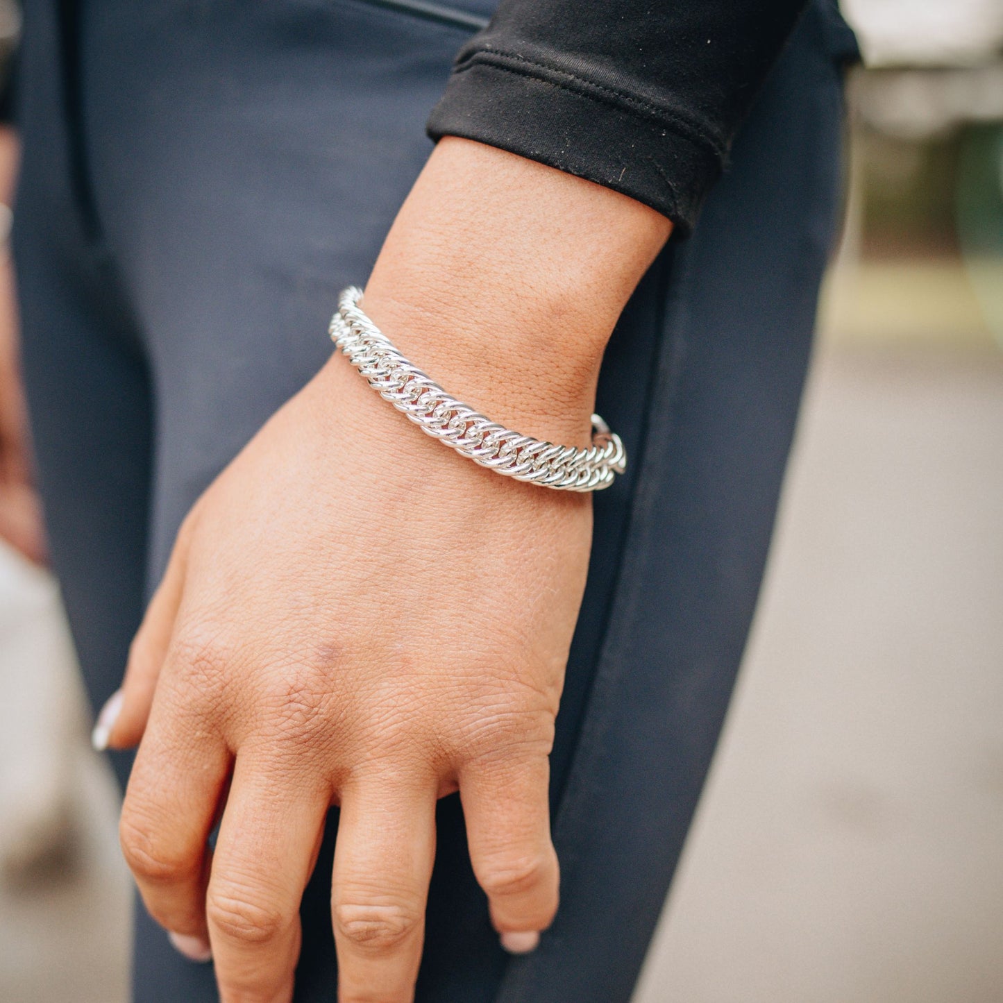 Equestrian hand wearing a silver curb chain bracelet with a blurred background.